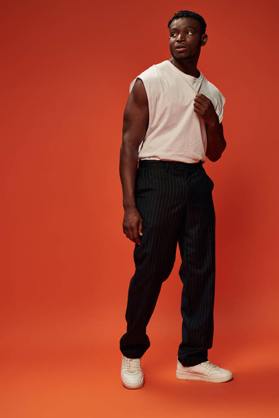 athletic african american man in black pants and white tank top looking away on red, full length - Fotografie, Obrázek