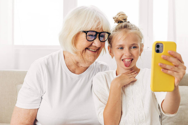 Называйте высшее образование в помещении диван фотографии счастье копия связи бабушка обнимает людей селфи семейное видео футболки взрослый космос белый внучка улыбается два телефона вместе ребенок - Фото, изображение