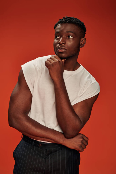 thoughtful african american male model in white tank top looking away while standing on red - Fotografie, Obrázek