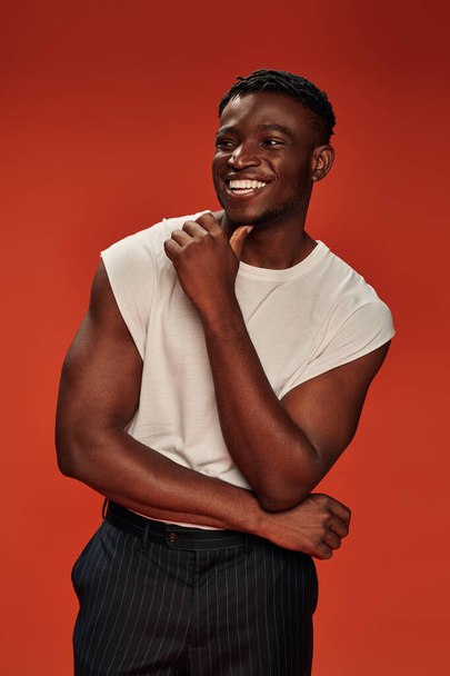 hombre afroamericano emocionado en ropa de calle elegante mirando hacia otro lado y riendo en rojo, vibraciones positivas - Foto, imagen
