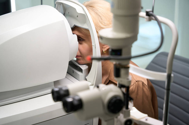 Mulher elegante senta-se na frente de um dispositivo oftálmico especial, uma senhora em uma consulta com um oftalmologista - Foto, Imagem
