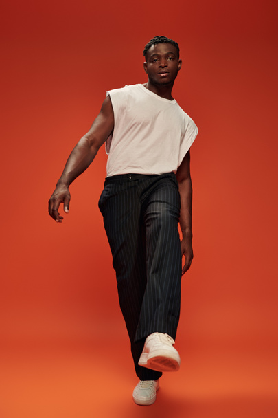 pełna długość charyzmatycznego i modnego afrykańskiego mężczyzny pozującego z rozciągniętą nogą na czerwono - Zdjęcie, obraz