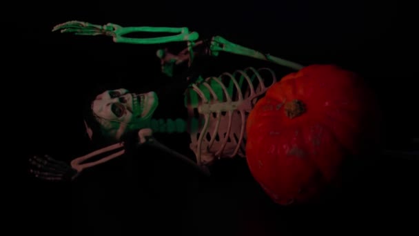Spielzeugskelettfigur neben orangefarbenem Kürbis auf schwarzem Hintergrund. Dekorationskonzept für Halloween. Schweden. - Filmmaterial, Video