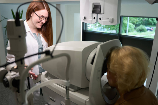 Frau in Freizeitkleidung beim Augenarzttermin, der Arzt benutzt ein modernes Gerät bei der Arbeit - Foto, Bild