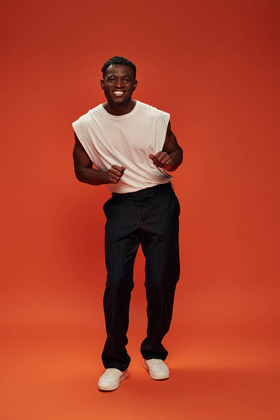 overjoyed african american man in fashionable casual clothes posing on red and orange backdrop - Foto, imagen