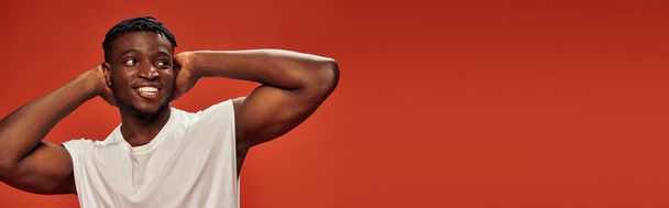 hymiö ja kuuma afrikkalainen amerikkalainen kaveri seisoo kädet pään takana ja katselee pois punainen, banneri - Valokuva, kuva