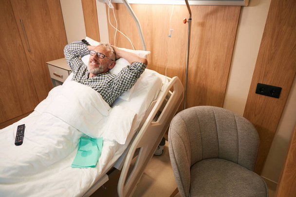 Paciente satisfeito está descansando após procedimentos em um quarto confortável, ele está localizado em uma cama especial - Foto, Imagem