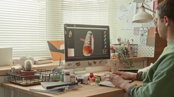 Panning pravý střední snímek muže běloch návrhář sedí za stolem v podkroví studio pracuje s počítačem, výběr barvy tenisky pro přizpůsobení - Záběry, video
