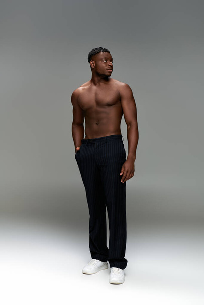 sportif homme afro-américain avec un corps fort et la main dans la poche regardant loin sur gris, pleine longueur - Photo, image