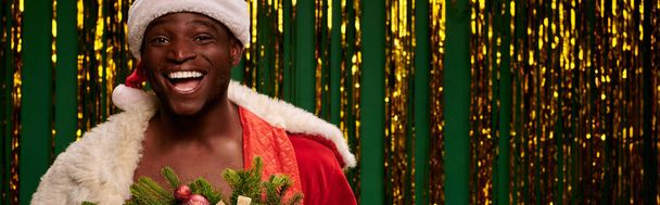 Unbekümmerter afrikanisch-amerikanischer Mann im Weihnachtskostüm bei goldenem Lametta auf grünem Grund lachend, Banner - Foto, Bild