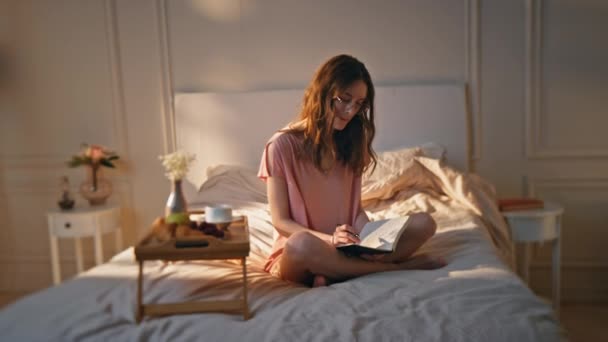 Creative woman making notes at home. Dreamy teenager writing diary in morning sunlight. Thoughtful inspired girl enjoy time alone sharing thoughts poetry in notebook. Pretty model planning wish list - Footage, Video