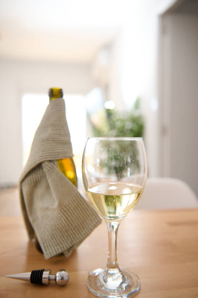 Csendélet egy borospohárral és egy üveg fehér pezsgővel a fa asztalon a nappaliban. Étel és ital fogyasztás. Reklámfelület másolása - Fotó, kép