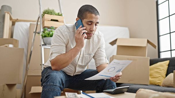 Mladý hispánec mluví po telefonu, dělá domácí účetnictví v novém domově - Fotografie, Obrázek