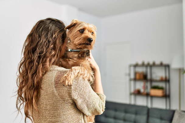 Mladý krásný hispánec žena objímání pes stojící doma - Fotografie, Obrázek