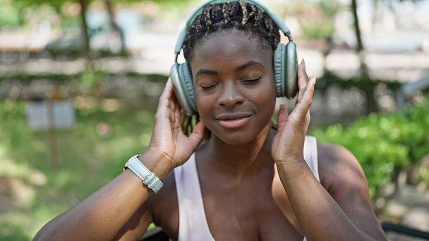 Müzik dinleyen Afrikalı Amerikalı kadın parkta bankta dinleniyor. - Fotoğraf, Görsel
