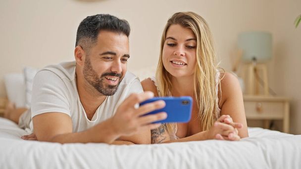 Άνδρας και γυναίκα ζευγάρι ξαπλωμένοι στο κρεβάτι χρησιμοποιώντας smartphone μιλώντας στο υπνοδωμάτιο - Φωτογραφία, εικόνα