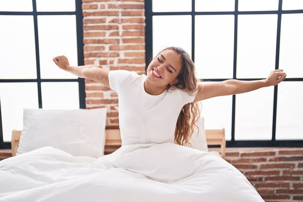 Fiatal, gyönyörű spanyol nő felébred kinyújtott karokkal a hálószobában. - Fotó, kép