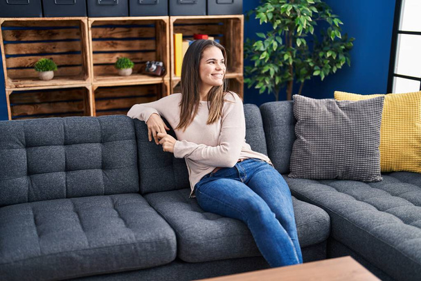 Nuori kaunis latino nainen hymyilee luottavainen istuu sohvalla kotona - Valokuva, kuva