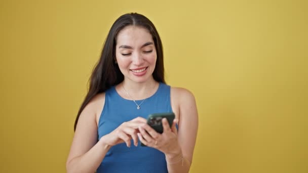 Jonge mooie Spaanse vrouw met behulp van smartphone glimlachen over geïsoleerde gele achtergrond - Video