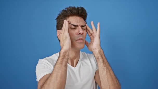 Hombre hispano joven que sufre de dolor de cabeza sobre un fondo azul aislado - Metraje, vídeo