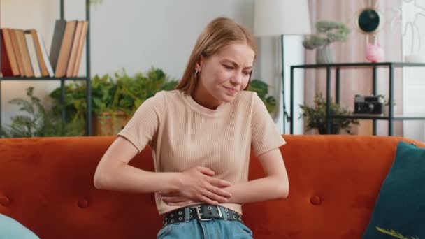 Chorą kobietę z bólem brzucha, skurcze miesiączkowe leżące na kanapie w domu. Dziewczyna trzymająca brzuch, odczuwająca ból brzucha lub miesiączki. Ból brzucha, zapalenie żołądka, biegunka, niestrawność - Materiał filmowy, wideo