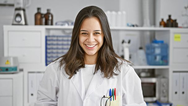 Hymyillen luottavaisesti, nuori ja kaunis latinonainen tiedemies seisoo hänen vilkkaan laboratorionsa sydämessä, täysin upotettuna hänen tiede- ja tutkimusmaailmaansa.. - Valokuva, kuva