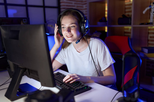 Joven mujer caucásica streamer jugando videojuego utilizando la computadora en la sala de juegos - Foto, Imagen