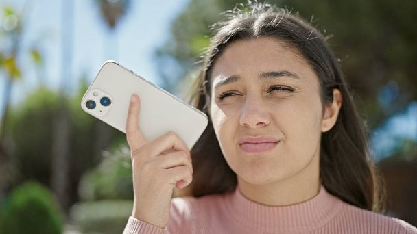Mladý krásný hispánec žena poslech audio zprávy u smartphonu s vážným výrazem v parku - Fotografie, Obrázek