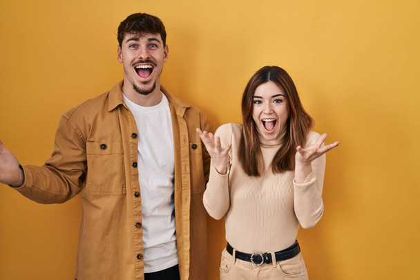 Sarı arka planda duran genç İspanyol çift çılgın ve başarıyı kollarını kaldırıp heyecanla haykırarak kutluyor. Kazanan konsept  - Fotoğraf, Görsel