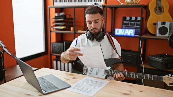 Fiatal arab férfi zenész játszik elektromos gitár zeneszerzés dal segítségével laptop zenei stúdióban - Fotó, kép