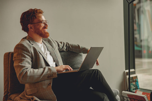 Красивий підприємець працює на ноутбуці, сидячи в сучасному коворкінгу в робочий день - Фото, зображення