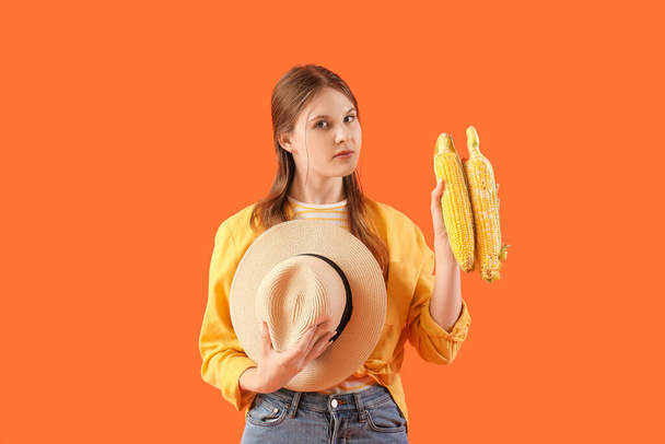 Mooie jonge vrouwelijke boer met rijpe maïskolven op oranje achtergrond - Foto, afbeelding