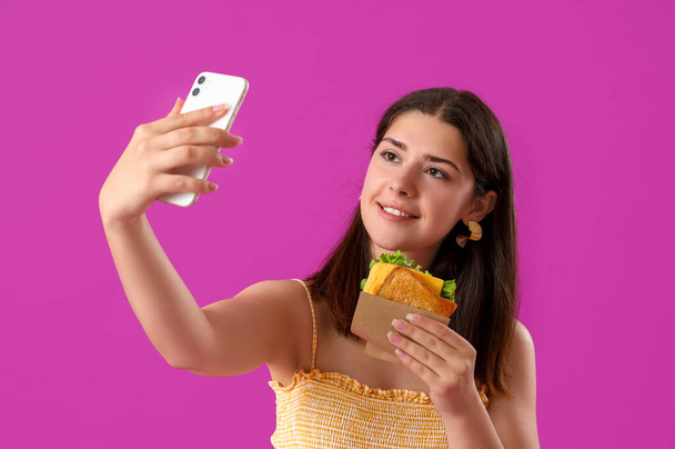 fiatal nő ízletes szendvics csinál szelfi lila háttér - Fotó, kép