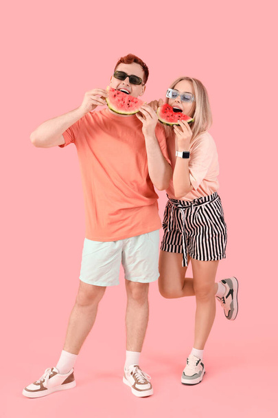 Jonge mooie man en vrouw in een zonnebril met plakjes verse watermeloen op roze achtergrond - Foto, afbeelding