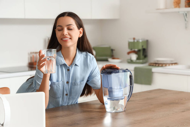 Beautiful young woman with water filter jug and glass in kitchen - Photo, Image