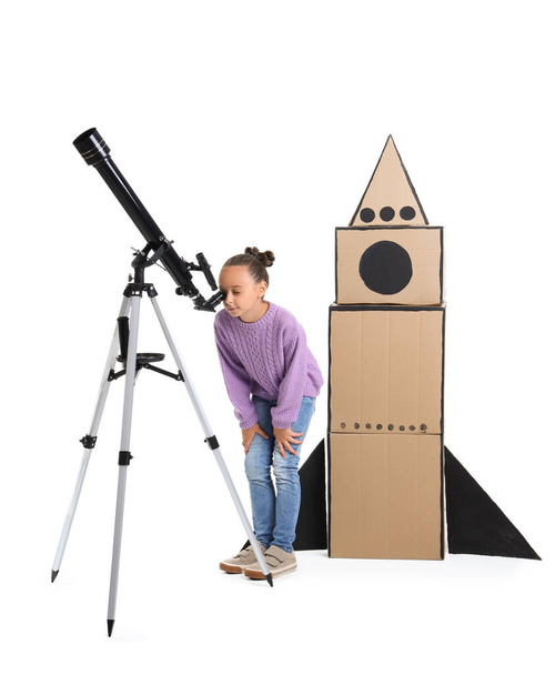 Teleskopu ve beyaz arka planda karton roketi olan sevimli küçük bir kız. - Fotoğraf, Görsel