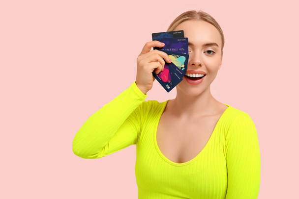 Mujer joven y bonita con tarjetas de crédito sobre fondo rosa - Foto, imagen