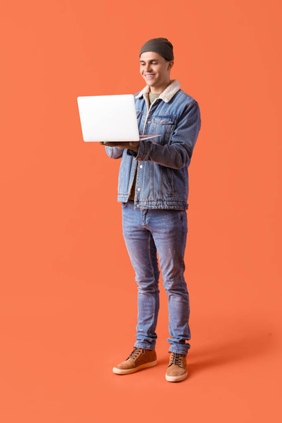 Jeune homme en vêtements d'hiver avec ordinateur portable sur fond orange - Photo, image