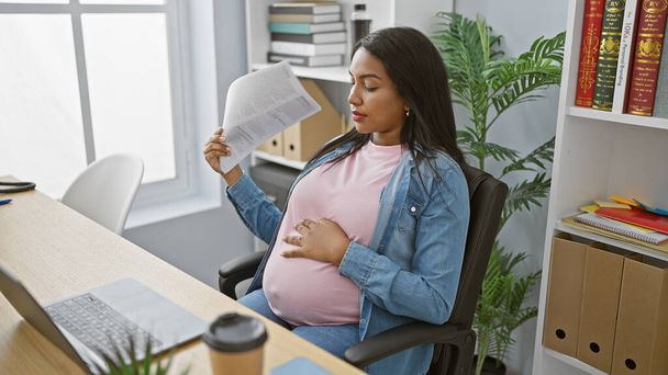 Young pregnant business woman, battling discomfort from the hot office, resorting to using documents as a handfan while immersed in demanding work. - Photo, Image