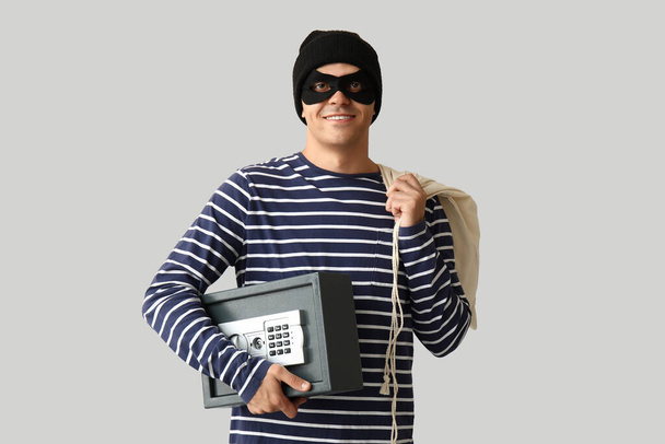 Ladrón macho con bolsa y caja fuerte sobre fondo gris - Foto, Imagen