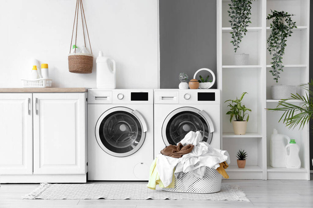 Cesta com roupas sujas perto de máquinas de lavar roupa na lavanderia - Foto, Imagem