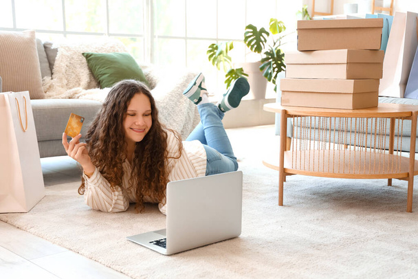 Kredi kartı, dizüstü bilgisayarı, çantaları ve kutuları olan genç bir kadın evde online alışveriş yapıyor. - Fotoğraf, Görsel