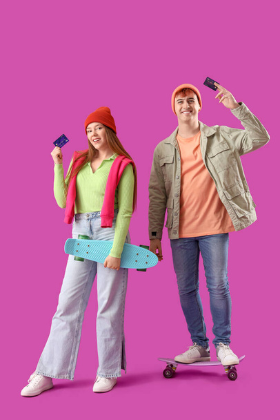 紫色の背景にクレジットカードを持つ若いカップル - 写真・画像