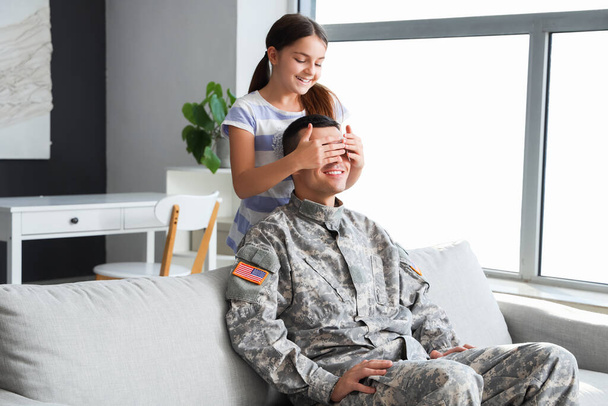 Niña cubriendo los ojos de su padre militar en casa. Celebración del Día de los Veteranos - Foto, Imagen
