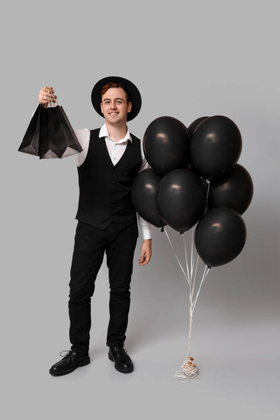 Nuori mies, jolla on ostoskasseja ja ilmapalloja harmaalla taustalla. Musta perjantai myynti - Valokuva, kuva