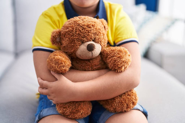 Adorable hispanic boy hugging teddy bear sitting on sofa at home - Foto, imagen