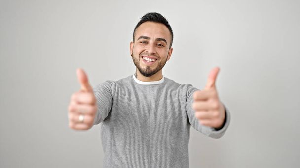 Латиноамериканець усміхається пальцями вверх по ізольованому білому фону. - Фото, зображення
