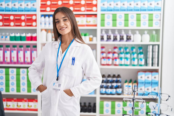 Young beautiful hispanic woman pharmacist smiling confident standing at pharmacy - 写真・画像