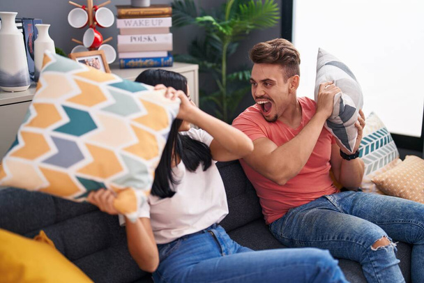 Мужчина и женщина улыбаются уверенно, дерутся с подушкой дома - Фото, изображение