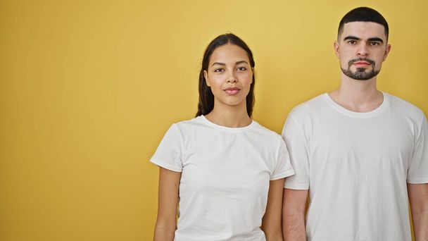 Belo casal de pé junto com rosto sério sobre fundo amarelo isolado - Foto, Imagem